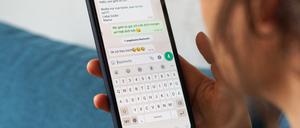 Eine junge Frau hält ihr Smartphone in der Hand und liest eine Whatsapp-Nachricht von ihrer Mama. 