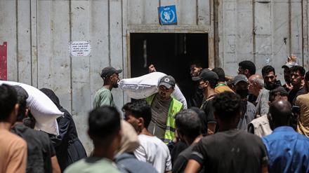 12.07.2025, Palästinensische Gebiete, Gaza: Palästinenser tragen Säcke mit Mehl weg, während andere vor einer vom Welternährungsprogramm der Vereinten Nationen (WFP) eingerichteten Verteilerstelle in Gaza-Stadt warten.