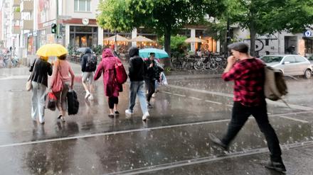 16.07.2025, Berlin: Fußgänger gehen mit Schirmen bei heftigem Regen über den Fußgängerübergang an der U-Bahn Haltestelle Schönhauser Allee.