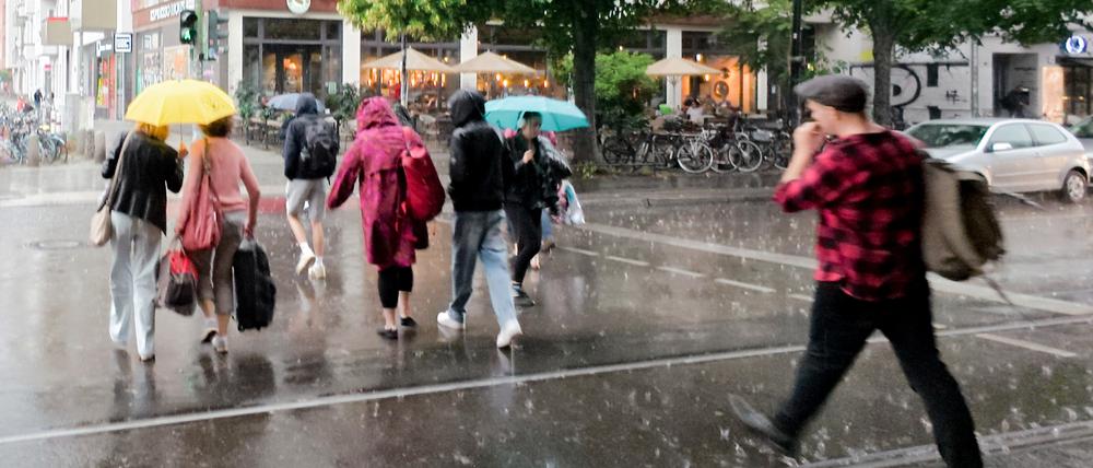 16.07.2025, Berlin: Fußgänger gehen mit Schirmen bei heftigem Regen über den Fußgängerübergang an der U-Bahn Haltestelle Schönhauser Allee.