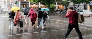 16.07.2025, Berlin: Fußgänger gehen mit Schirmen bei heftigem Regen über den Fußgängerübergang an der U-Bahn Haltestelle Schönhauser Allee.