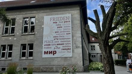 Das Wort Frieden, übersetzt in mehrere Sprachen, hängt an der Außenwand des Canisius Kollegs“.