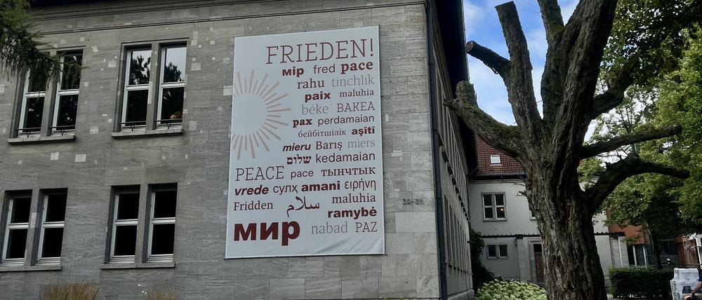 Das Wort Frieden, übersetzt in mehrere Sprachen, hängt an der Außenwand des Canisius Kollegs“.
