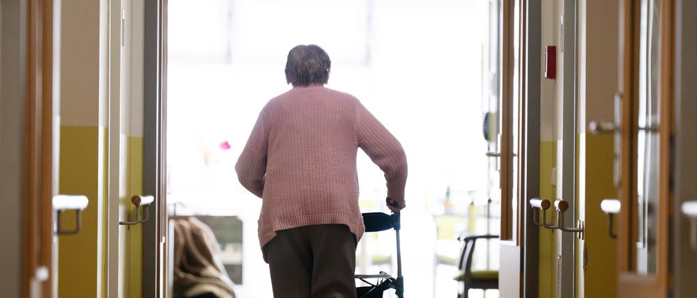 Eine Frau geht mit einem Rollator in einem Altenheim auf einem Gang entlang.