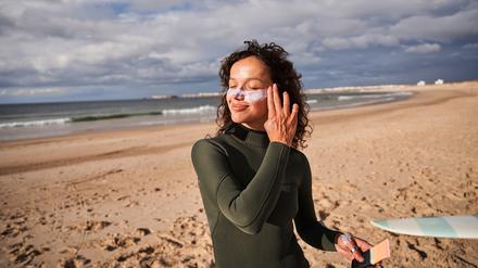 Eine junge Frau am Strand cremt sich das Gesicht ein. 