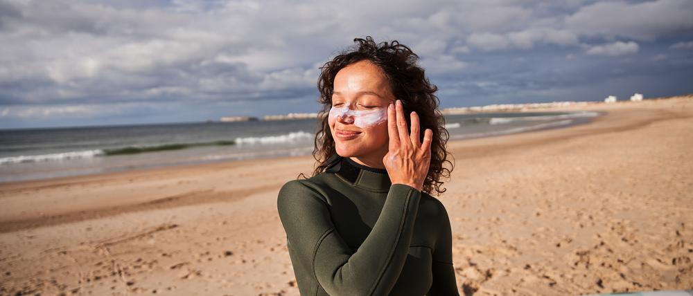 Eine junge Frau am Strand cremt sich das Gesicht ein.