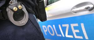 Ein Polizist mit Handschellen und einer Pistole am Gürtel steht vor einem Streifenwagen. (Symbolbild)