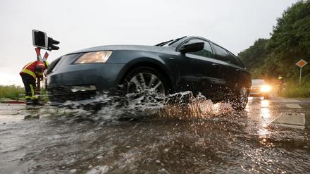  Baden-Württemberg, Riedlingen: Einsatzkräfte der Feuerwehr sind nach einem Unwetter an einem überfluteten Bahnübergang im Einsatz, während Autos durch das Wasser fahren. 