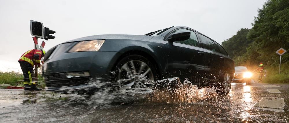  Baden-Württemberg, Riedlingen: Einsatzkräfte der Feuerwehr sind nach einem Unwetter an einem überfluteten Bahnübergang im Einsatz, während Autos durch das Wasser fahren. 