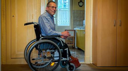Michael Starke im Rollstuhl in der Diele seiner Mietwohnung, er trägt spezielle orthopädische Schuhe. 