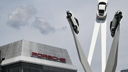 Der Schriftzug von Porsche ist an einem Gebäude am Stammsitz angebracht. Rechts daneben sind Porsche-Fahrzeuge an einem Kunstwerk auf dem Porscheplatz angebracht. 