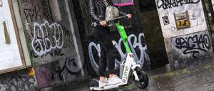 Eine Person fährt auf einem E-Scooter mit einem Regenschirm.