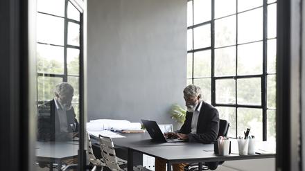 Ein älterer Mann sitzt allein im Büro an einem Schreibtisch.