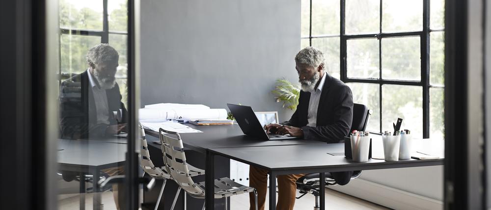 Ein älterer Mann sitzt allein im Büro an einem Schreibtisch.