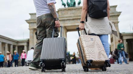 Zwei Touristen stehen mit ihren Trolleys vor dem Brandenburger Tor. Berlin ist für viele Reisende ein beliebtes Reiseziel. 