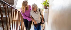 Eine jüngere Frau hilft einer alten Frau die Treppe hinauf. 
