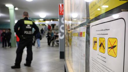 Ein Polizeibeamter steht am Bahnhof Alexanderplatz zu Beginn des Waffenverbots in Berliner U-Bahnen neben einem Hinweisschild auf das Waffenverbot.