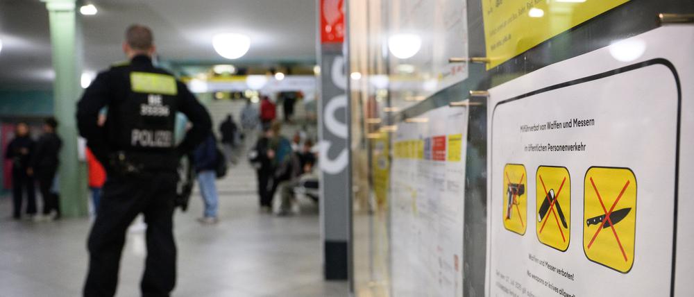 Ein Polizeibeamter steht am Bahnhof Alexanderplatz zu Beginn des Waffenverbots in Berliner U-Bahnen neben einem Hinweisschild auf das Waffenverbot.