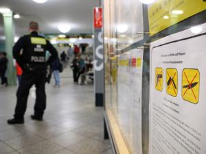 Ein Polizeibeamter steht am Bahnhof Alexanderplatz zu Beginn des Waffenverbots in Berliner U-Bahnen neben einem Hinweisschild auf das Waffenverbot.