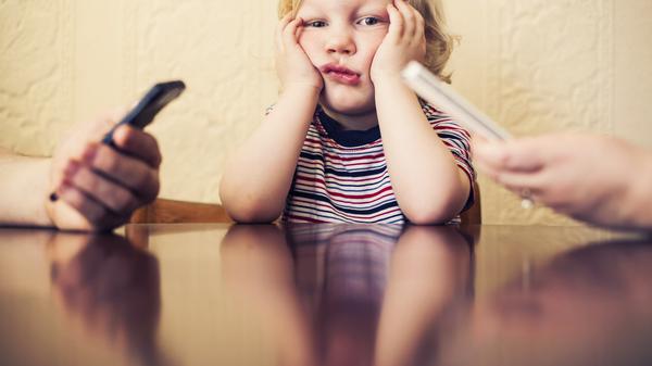 Eltern tippen, wischen, lesen, während das Kind aufblickt und wartet. Was alltäglich wirkt, kann die frühe Entwicklung von Kindern stören.