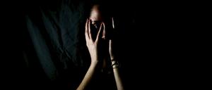 Eine Frau im Dunkeln (Symbolbild für häusliche Gwalt). 