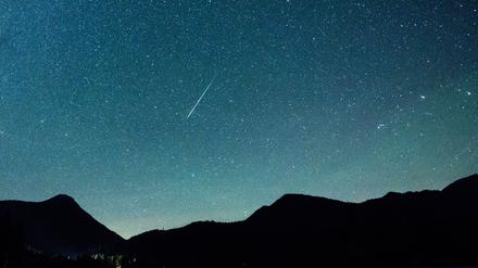 Eine Sternschnuppe leuchtet vor der Milchstraße am Himmel über dem Walchensee. 