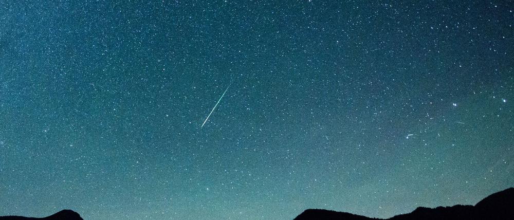 Eine Sternschnuppe leuchtet vor der Milchstraße am Himmel über dem Walchensee.