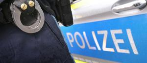 Ein Polizist mit Handschellen und einer Pistole am Gürtel steht vor einem Streifenwagen. 