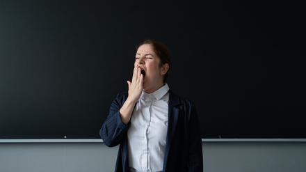 Eine gähnende Lehrerin steht an der Tafel.