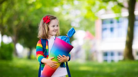 Ein Kind in einer bunten Jacke hält eine Schultüte in allen Farben des Regenbogens.