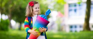 Ein Kind in einer bunten Jacke hält eine Schultüte in allen Farben des Regenbogens.