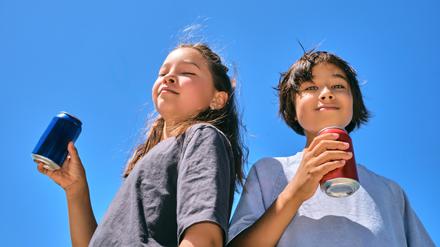 Zwei Kinder trinken Drinks aus bunten Dosen.