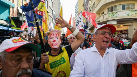 Straßenverkäufer marschieren mit Masken und Fahnen über die bekannte Rua 25 de Março, um gegen die US-Regierung unter Präsident Trump zu protestieren. 