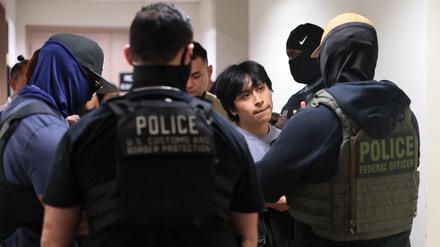Polizeibeamte eskortieren eine Person, die zur Immigrationsbehörde gebracht wird. 