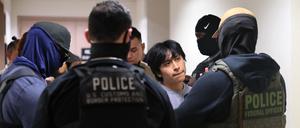 Polizeibeamte eskortieren eine Person, die zur Immigrationsbehörde gebracht wird. 