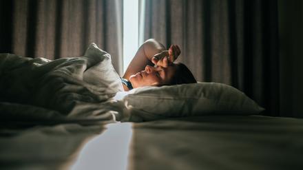 Eine junge Frau liegt in einem abgedunkelten Zimmer auf dem Bett.