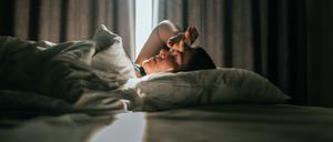 Eine junge Frau liegt in einem abgedunkelten Zimmer auf dem Bett.