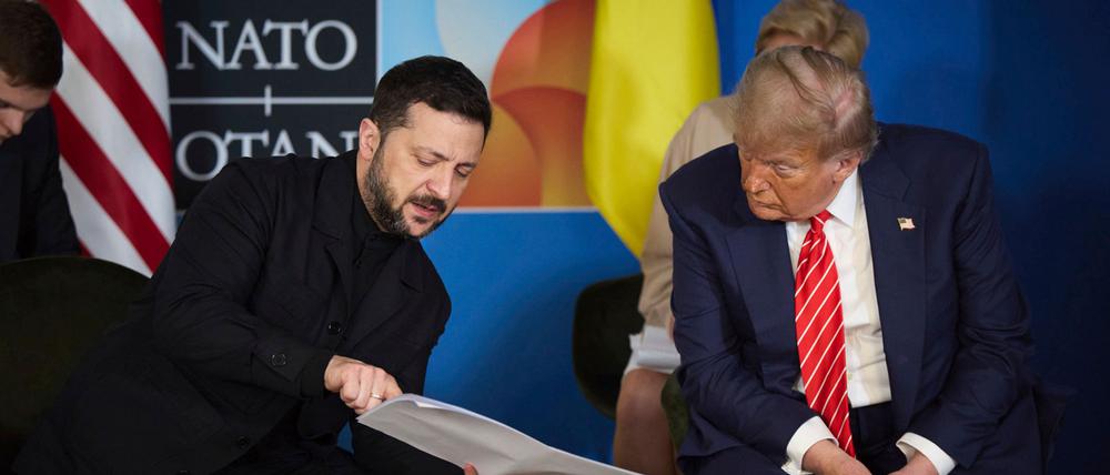 Der ukrainische Präsident Wolodymyr Selenskyj zeigt US-Präsident Donald Trump (r) während ihres Treffens am Rande des NATO-Gipfels einige Dokumente. 