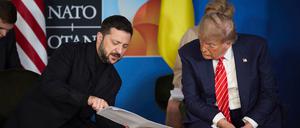 Der ukrainische Präsident Wolodymyr Selenskyj zeigt US-Präsident Donald Trump (r) während ihres Treffens am Rande des NATO-Gipfels einige Dokumente. 