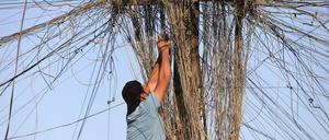 Ein Mann verbindet elektrische Leitungen, die zwischen Gebäuden in einer Straße in der Sadr City hängen.