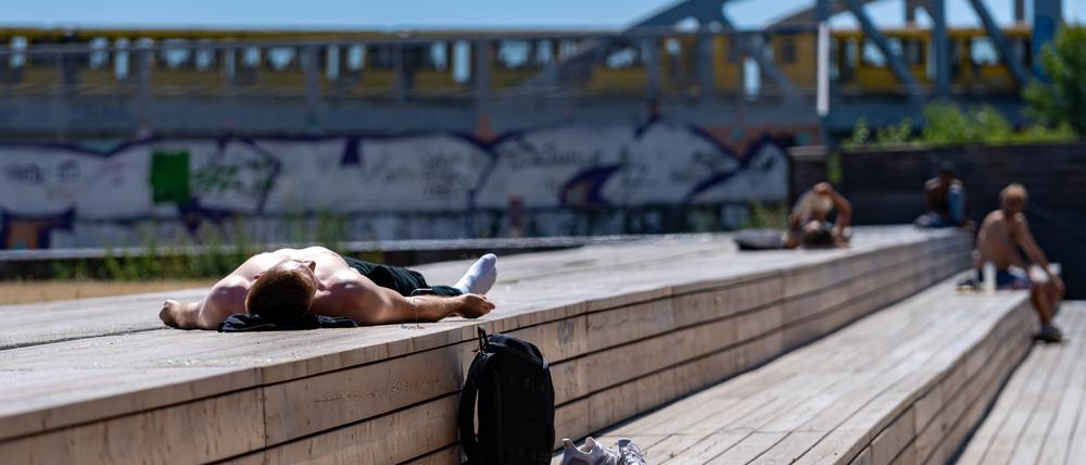 Eine Person sonnt sich auf Holzbalken. Im Hintergrund eine U-Bahn der BVG. Am Gleisdreieck Park. Berlin, 30.06.2025. Berlin Deutschland *** A person sunbathing on wooden beams In the background a BVG underground train Am Gleisdreieck Park Berlin, 30 06 2025 Berlin Germany Copyright: xTiloxStraussx