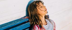 Eine junge Frau sitzt entkräftet und verschwitzt auf einer Bank.