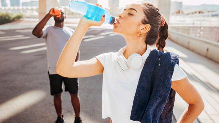 Zwei Sportler trinken aus einer Plastikflasche.