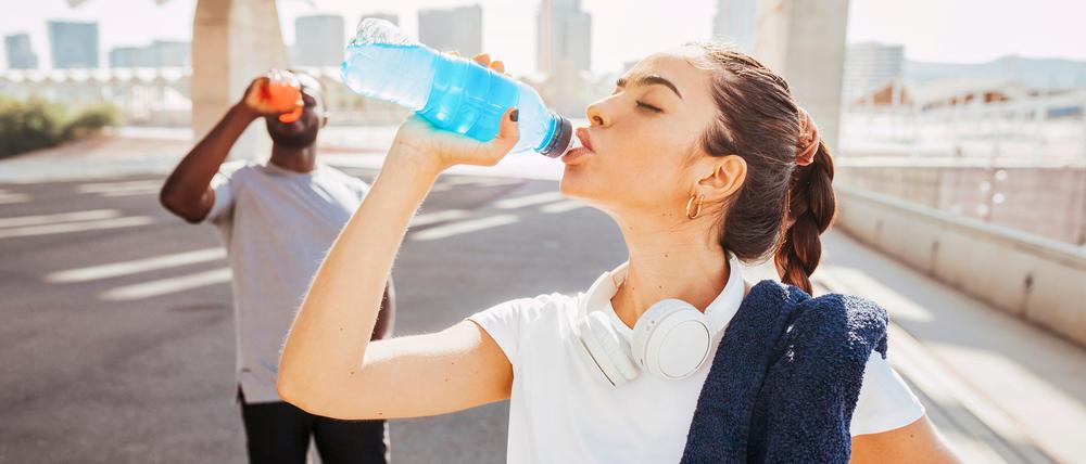 Zwei Sportler trinken aus einer Plastikflasche.