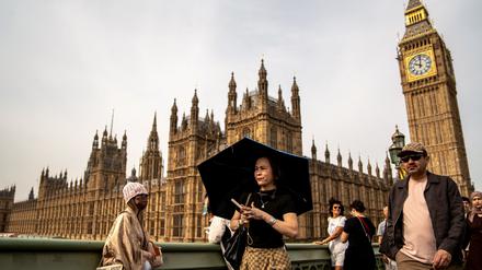 Eine Person schützt sich vor der Sonne unter einem Regenschirm, während sie auf der Westminster Bridge vor dem Hintergrund des Elizabeth Towers spazieren geht, der allgemein unter dem Namen der Glocke der Uhr „Big Ben“ im Zentrum Londons bekannt ist (Symbolbild).