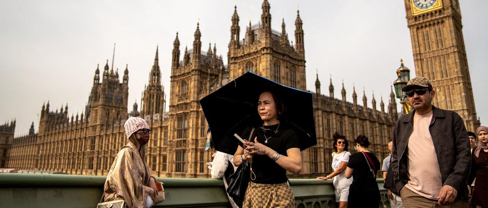 Eine Person schützt sich vor der Sonne unter einem Regenschirm, während sie auf der Westminster Bridge vor dem Hintergrund des Elizabeth Towers spazieren geht, der allgemein unter dem Namen der Glocke der Uhr „Big Ben“ im Zentrum Londons bekannt ist (Symbolbild).