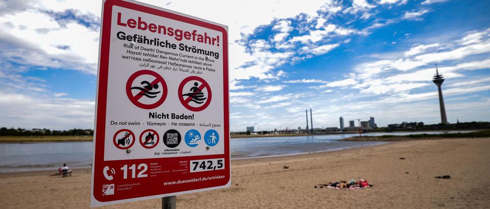 Ein Hinweisschild am Paradiesstand in Düsseldorf weist auf die Gefahren beim Schwimmen im Rhein hin.
