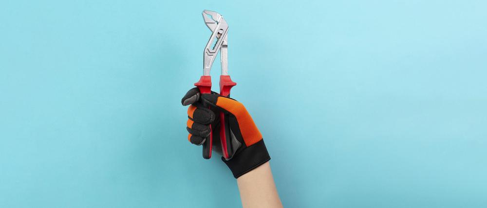 Zu sehen ist eine Hand mit Arbeitshandschuh vor blauem Hintergrund, die eine Zange hält.