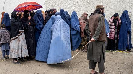 Ein Taliban-Sicherheitsbeamter steht Wache, während afghanische Frauen in Burka mitten im Regen in einer Schlange warten, um während des heiligen islamischen Fastenmonats Ramadan gespendete Lebensmittel in Kabul am 25. März 2025 entgegenzunehmen.