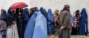 Ein Taliban-Sicherheitsbeamter steht Wache, während afghanische Frauen in Burka mitten im Regen in einer Schlange warten, um während des heiligen islamischen Fastenmonats Ramadan gespendete Lebensmittel in Kabul am 25. März 2025 entgegenzunehmen.